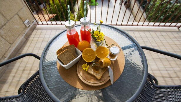 A round glass table with a metal frame, a white tray with toast, orange slices, a small bowl of jam, and two bottles of red drink with straws. - Casa Borgo Regina B&B Bari (Noicattaro)
