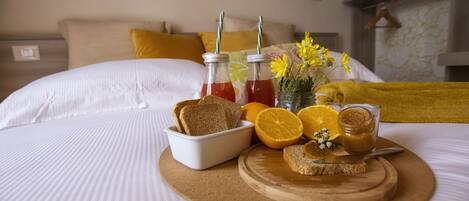 A neatly made bed with a breakfast tray containing toast, orange slices, and a jar of jam.
