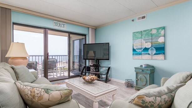 Una sala de estar con televisor, una mesa con cesta y un sofá. Hay un cartel en la pared que dice "BEACH".