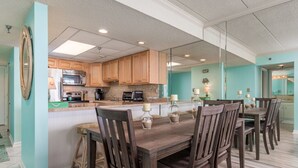 Una cocina con armarios de madera, una isla central con un lavamanos y una zona de comedor con mesa y sillas de madera.