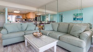 Una sala de estar con un sofá verde claro, una mesa de centro blanca y una cocina al fondo.