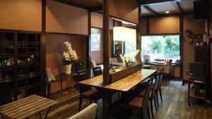 A dining area with a wooden table and chairs, a potted plant, and a view of the outdoors. - Ikariya Ryokan (Yamanouchi)
