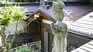 A traditional Japanese building with a wooden roof and a stone statue of a deity. - Ikariya Ryokan (Yamanouchi)