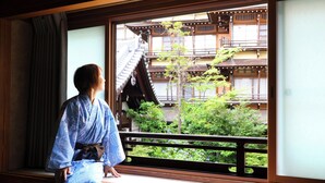 A traditional Japanese room with tatami flooring, a sliding door, and a view of a traditional building with wooden balconies. - Ikariya Ryokan (Yamanouchi)