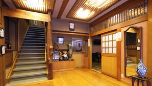 A wooden interior with a staircase, wooden flooring, and a small table with a vase. - Ikariya Ryokan (Yamanouchi)