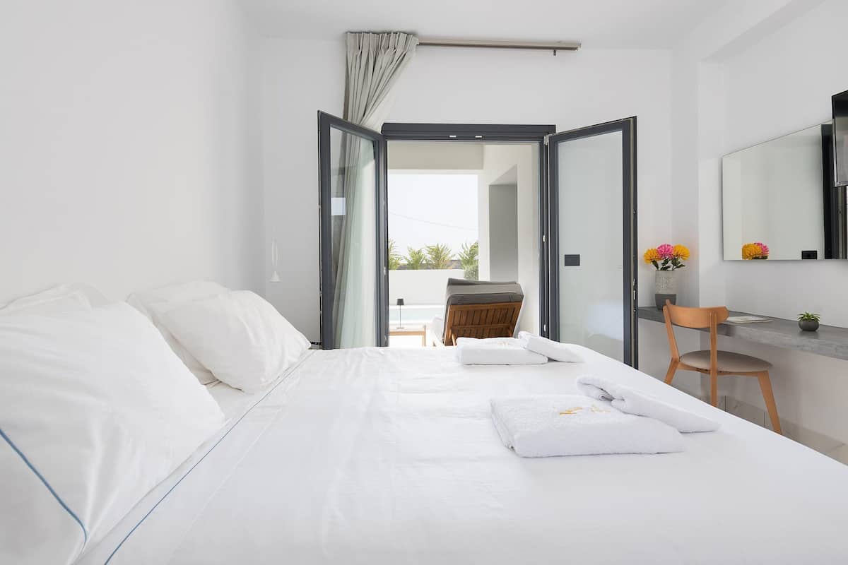 A modern hotel room with a large bed, a desk, a chair, and a view of the outdoors.