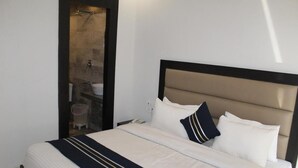 A neatly made bed with white bedding and a navy blue accent, a headboard, and a small bedside table with a lamp.