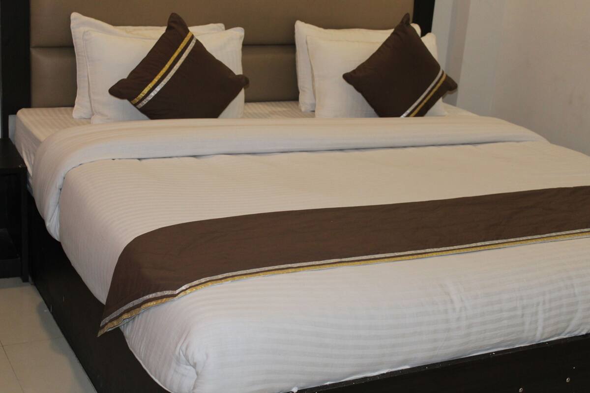 A neatly made bed with white linens and brown pillows, a dark headboard, and a brown throw blanket.