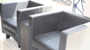 Three black armchairs with a smooth surface, positioned in a row against a white wall.