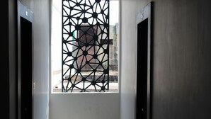 An interior view of a hotel room with a geometric patterned window, a white wall, and a door on the right.