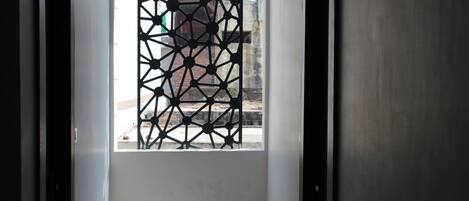 Ein Blick ins Hotelzimmer. Es zeigt ein geometrisches Muster am Fenster, eine weiße Wand und eine Tür auf der rechten Seite.