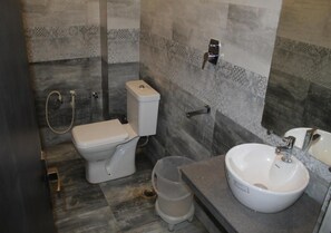 Une salle de bain équipée de toilettes, d’un bidet, d’un lavabo et d’une poubelle.