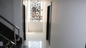 A modern hallway with a staircase, a geometric window, and a clean, tiled floor.