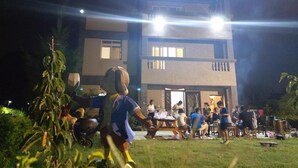A building with multiple floors and a flat roof, surrounded by a grassy area with people gathered around tables. - Kinmen Good Places (Jinning)