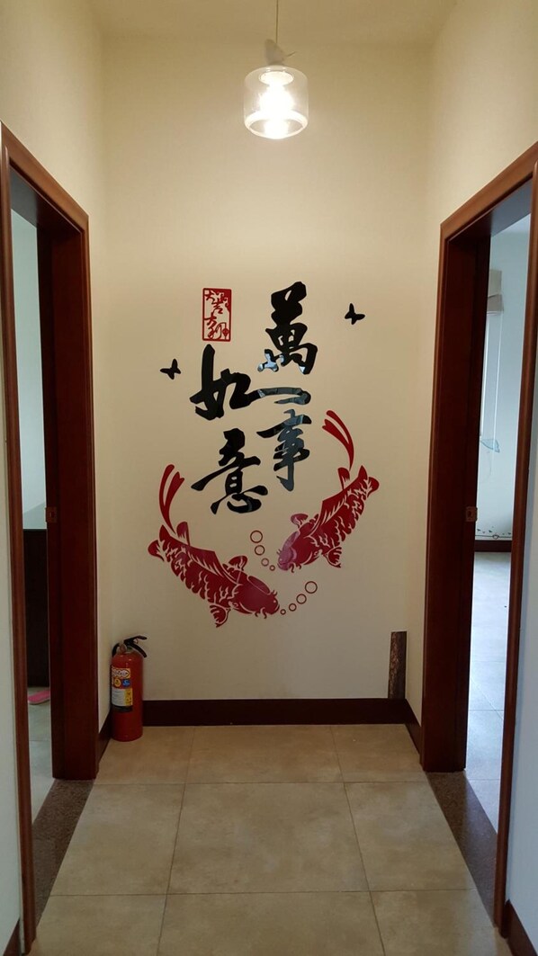 A hallway with a ceiling light, a fire extinguisher, and a wall with Chinese calligraphy and red artwork.