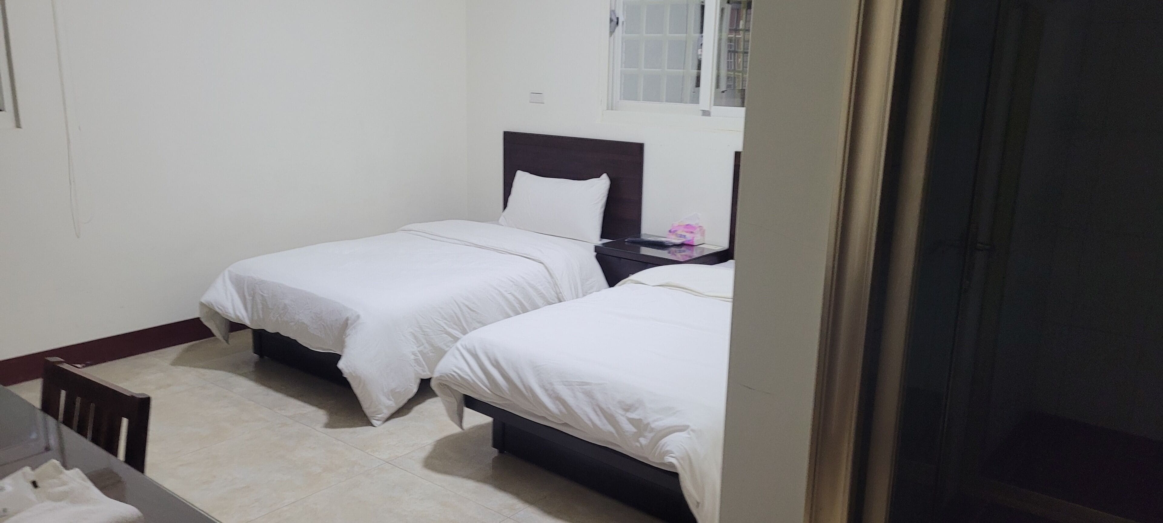 Quarto pequeno e limpo com duas camas, uma mesa e uma cadeira.