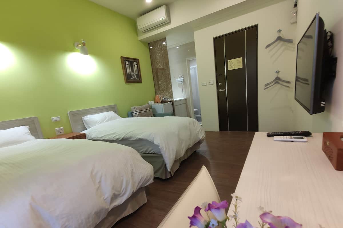 A hotel room with two beds, a desk, a TV, and a wardrobe.