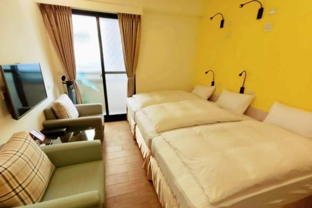A hotel room with two beds, a sofa, a TV, and a window with curtains.