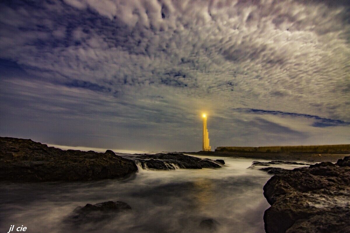 A coastal landscape with a prominent lighthouse, rocky terrain, and a body of water.
