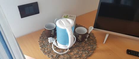 A desk with a coffee maker, two coffee mugs, a remote control, and a computer monitor.