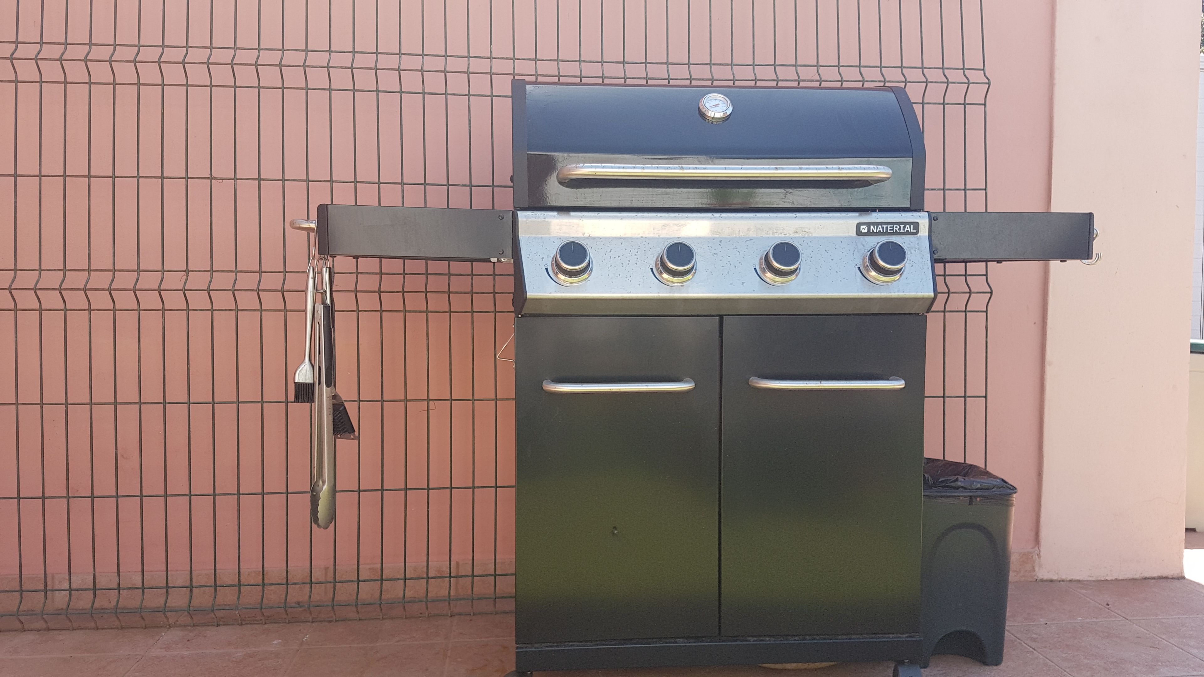 Een Naterial grill voor buiten met vier branders, een bijzettafel en een opbergvak aan de voorzijde.