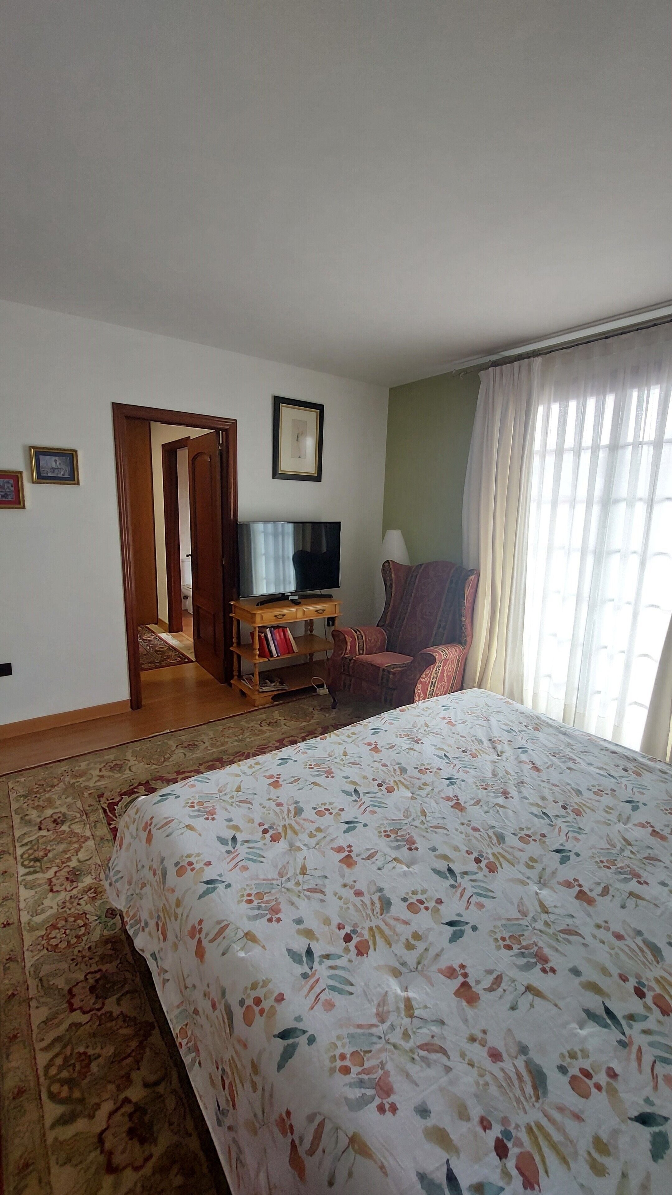 A hotel room with a large bed, a television, a chair, and a door leading to another room.