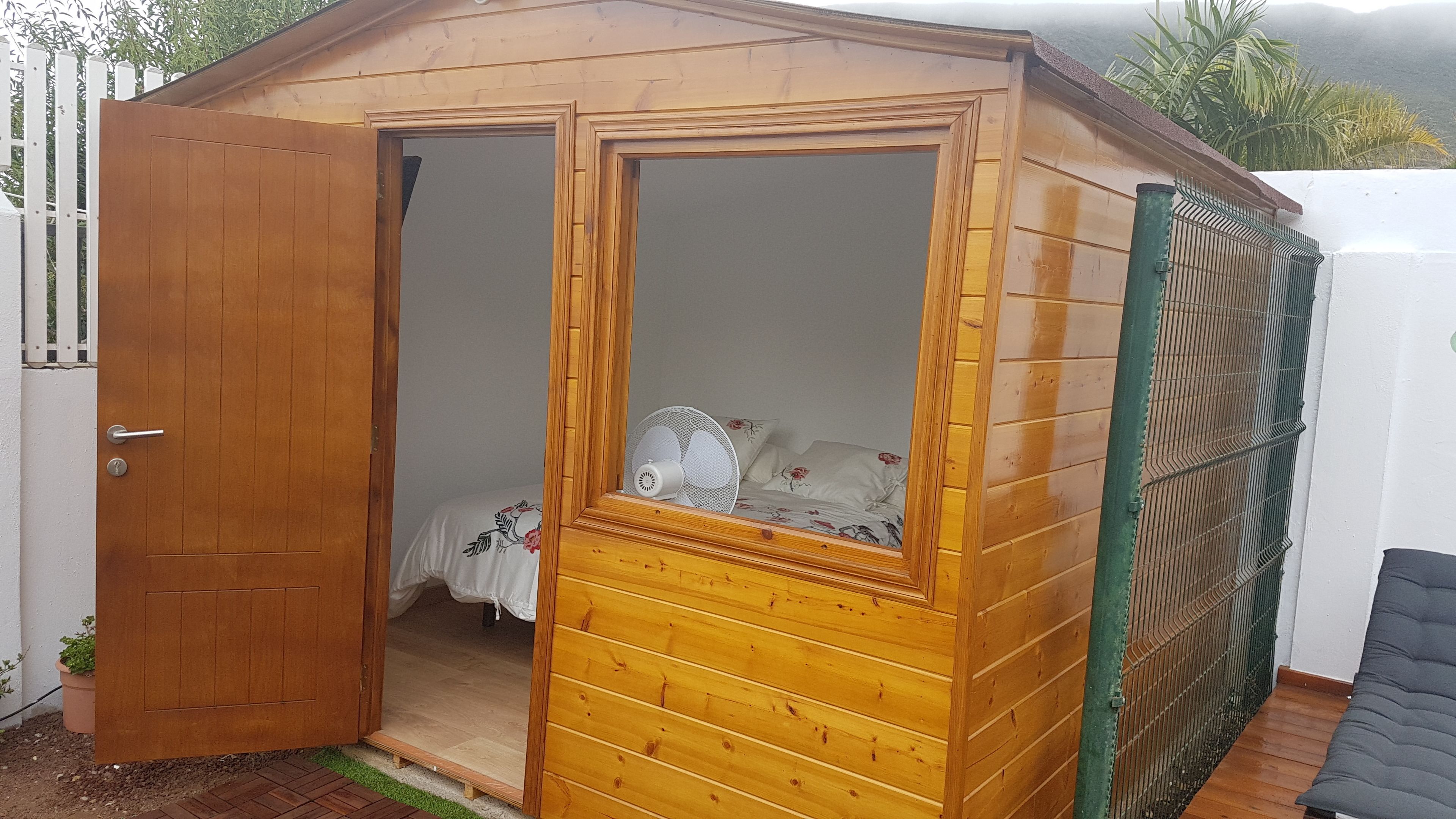 Un cobertizo de madera con una puerta, una ventana y una cama en su interior.