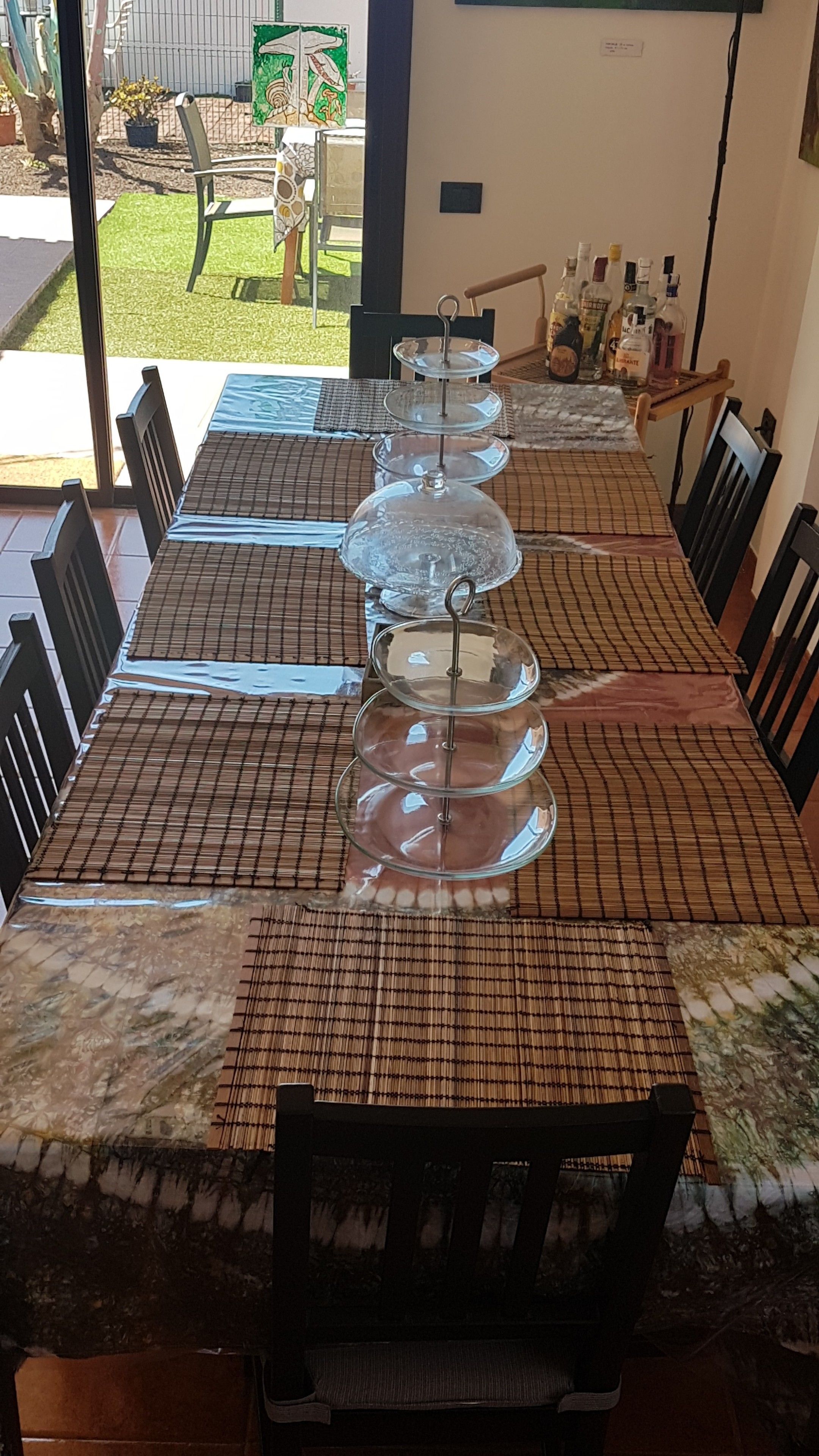 Una mesa de comedor con un expositor de vidrio de tres niveles en el centro, rodeada de sillas y un mantel individual.