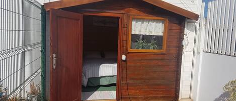 A small wooden cabin with a single bed and a window.