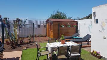 A patio with a table and chairs, a wooden shed, and a white wall with a mural.