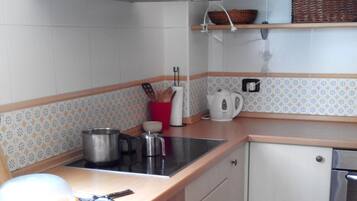 Una cocina compacta con armarios blancos, una campana extractora de acero inoxidable, un lavamanos y una cafetera.