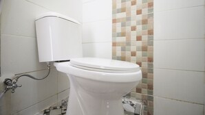 A white toilet with a tank and a wall-mounted flush handle. - OYO 654 Fabio Guest House Syariah (Bandar Lampung)
