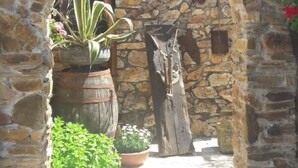Un arco de piedra que da acceso a un patio con macetas y un poste de madera rústico.