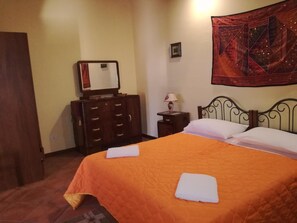 A hotel room with a bed, a dresser, a mirror, a lamp, and a tapestry on the wall. - Tenute Margana (Calatafimi)