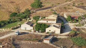 Vista aérea de una propiedad rural con edificios de piedra, un camino pavimentado y vegetación circundante.