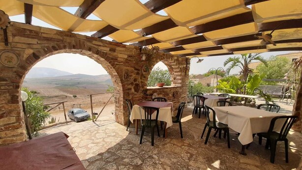 Un patio al aire libre con paredes de piedra, mesas y sillas, con vistas a un paisaje pintoresco.