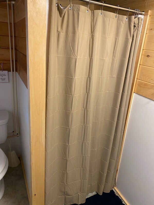 A bathroom with a beige shower curtain, wooden walls, a white toilet, and a wooden cabinet. - Waterfront, Rustic Cabin, Great Swimming, Own Dock, Raft (Tully)