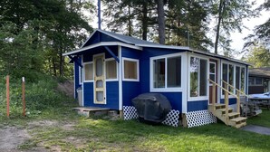 Eine kleine, eingeschossige Holzhütte mit Veranda, überdachter Grillstation und einer Holztreppe.