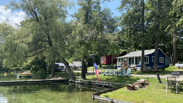 Eine Blockhütte am See mit Steg, klarem Wasser und einer Flagge.