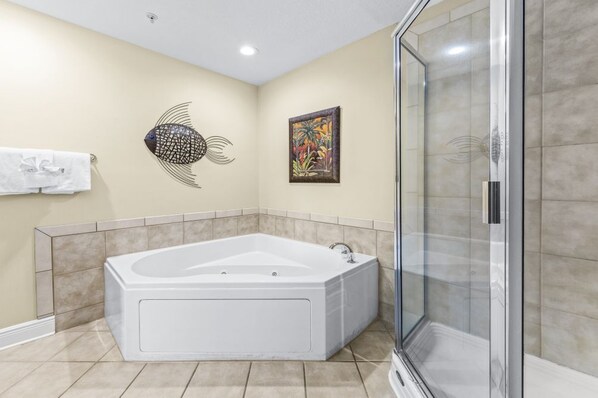 Un baño con una bañera grande, cabina de ducha con mampara de vidrio, toallero y dos obras de arte colgadas en la pared.