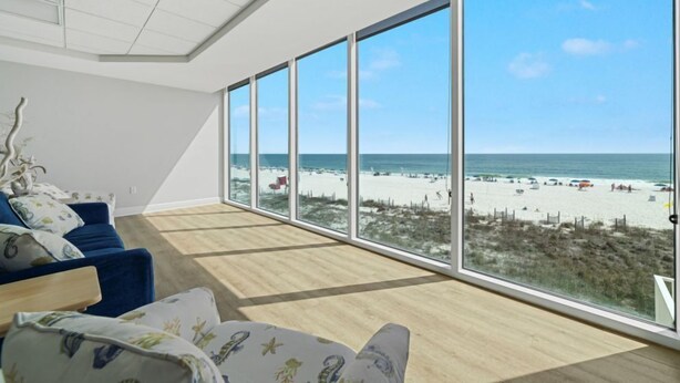 Una habitación con un amplio ventanal con vista a la playa, un sofá azul y piso de madera.