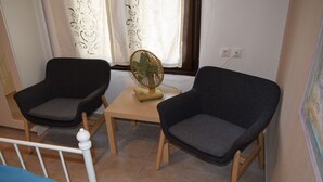 Una habitación con dos sillones grises oscuros, una mesita de madera y un ventilador de pie.