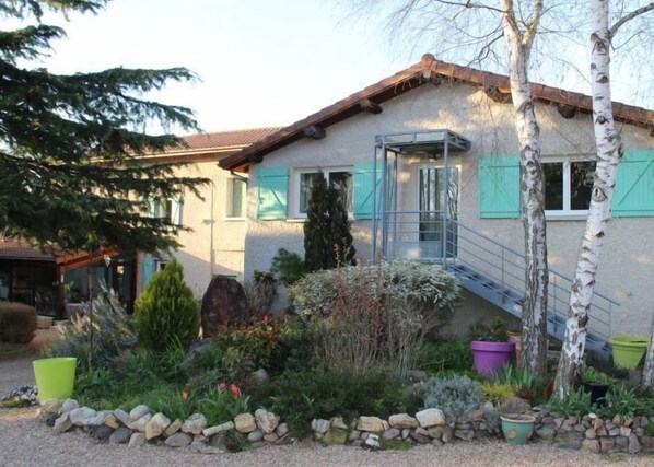 Una casa de fachada de piedra, techo de madera y un pequeño jardín con diversas plantas y un sendero de piedra.