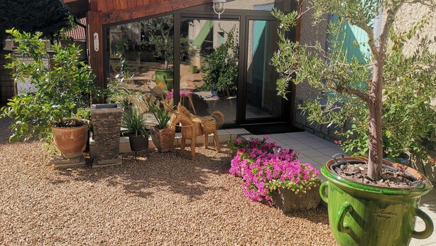 A patio area with potted plants, a wooden pergola, and a glass door leading to a garden. - La Ferme de Capucine (Culhat)