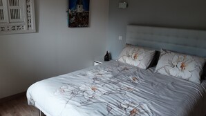 A bedroom with a bed, a nightstand, a wall-mounted painting, and a decorative wall panel. - La Ferme de Capucine (Culhat)