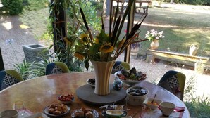 A round dining table with various dishes, a vase with flowers, and a view of a garden with a statue. - La Ferme de Capucine (Culhat)