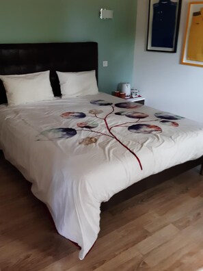 Una cama bien tendida con una colcha estampada con motivos florales, un cabecero oscuro y piso de madera.