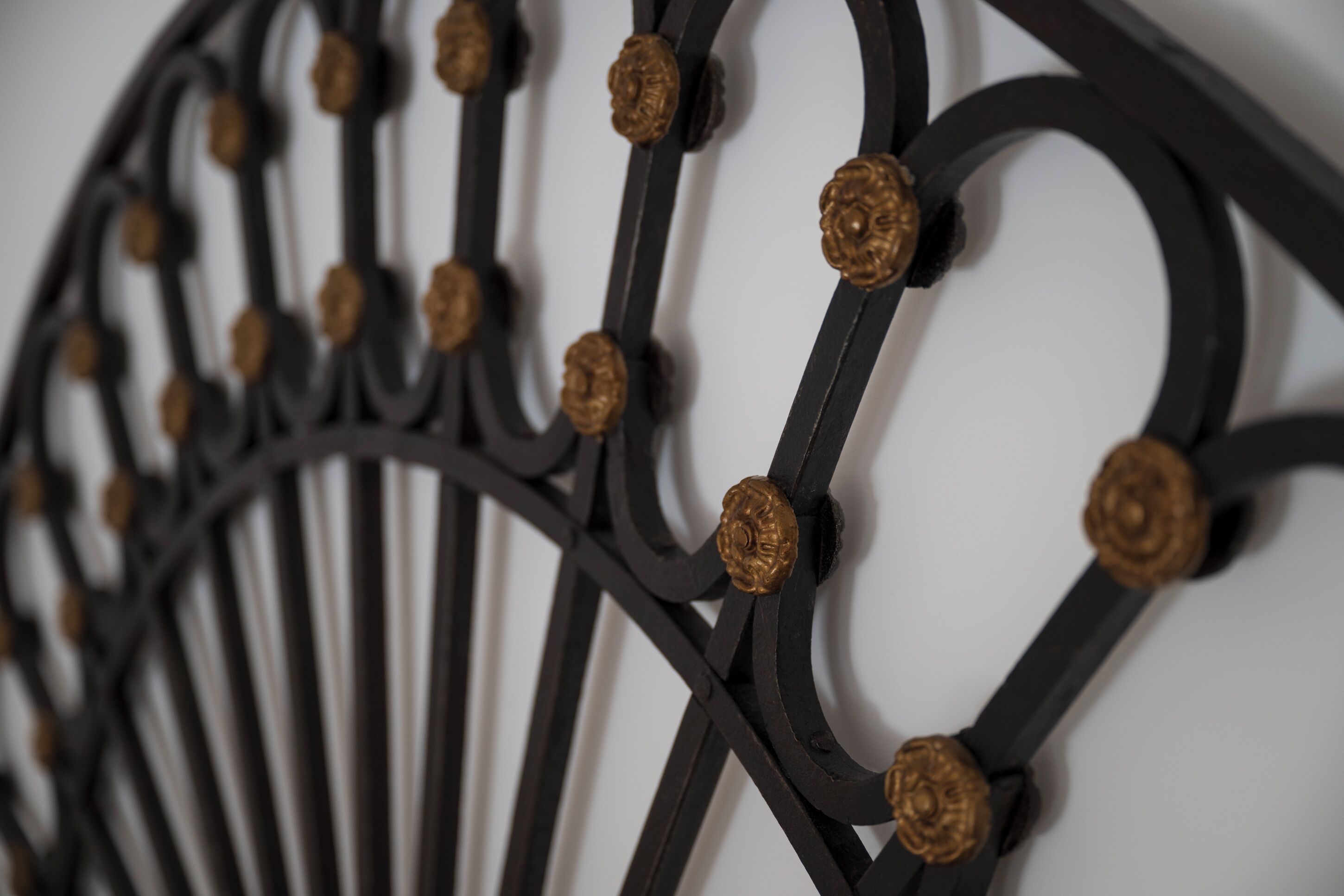 Een close-up van een metalen hekwerk met gedetailleerde, ronde versieringen en een reeks gelijkmatig verdeelde, goudkleurige elementen.