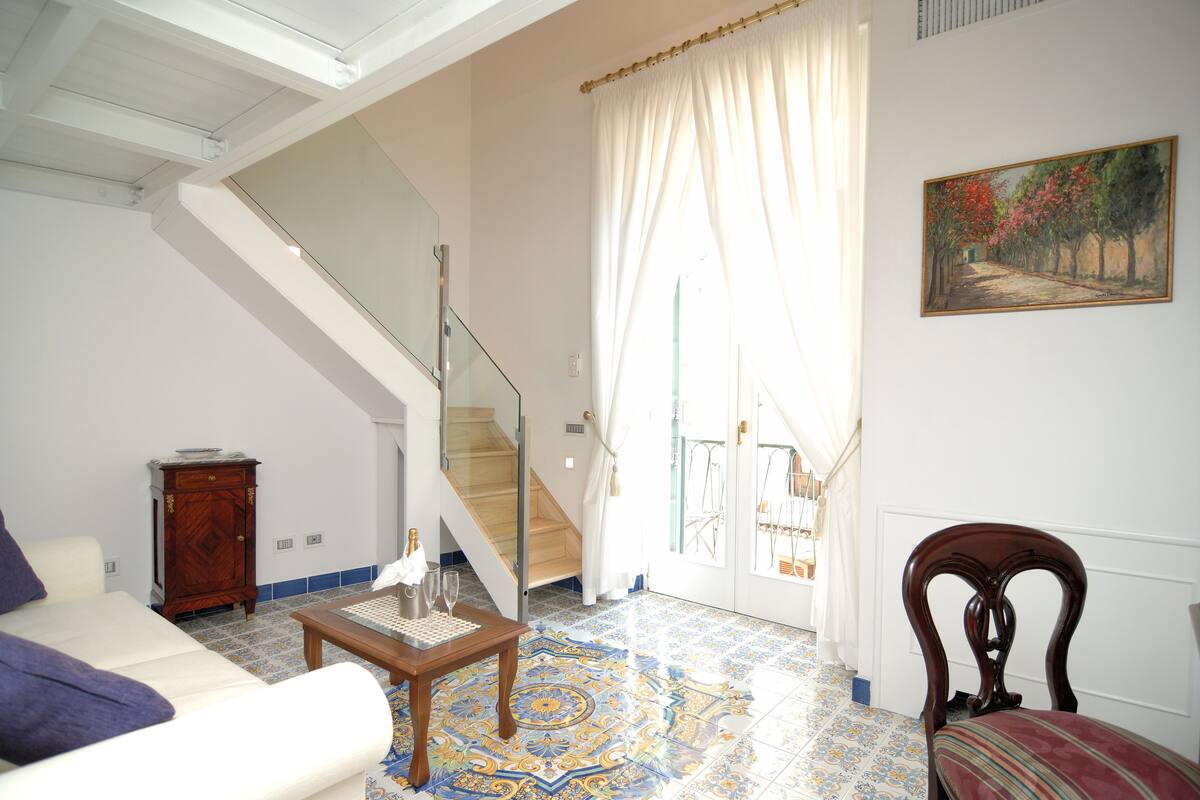 A living room with a sofa, a coffee table, a chair, a staircase, and a painting on the wall.
