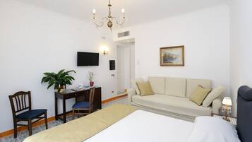 Ein Hotelzimmer mit einem Bett, einer Couch, einem Schreibtisch mit Stuhl, einem Fernseher, einer Topfpflanze und einem Kronleuchter.